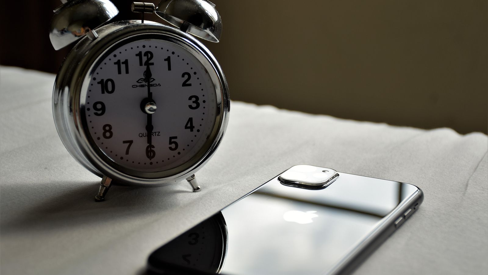 Relógio despertador prateado ao lado de um smartphone